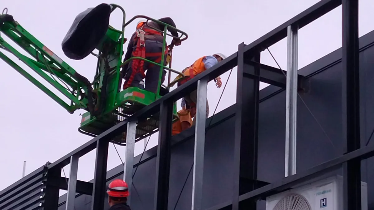 Trabajadores sobre una plataforma elevadora junto a los paneles oscuros de la fachada del aeropuerto.