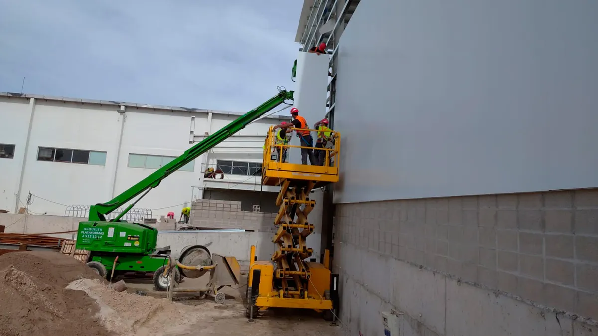 Trabajadores en plataformas elevadoras junto a los paneles claros de la fachada de Bader.