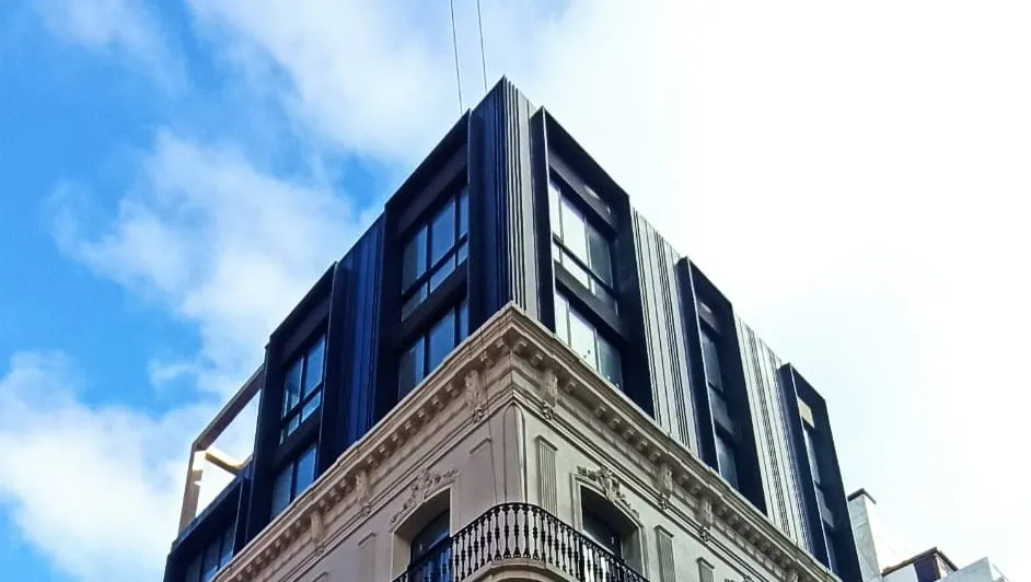 Vista desde la calle del Edificio Maldonado, con revestimiento oscuro en los niveles superiores y fachada existente debajo.