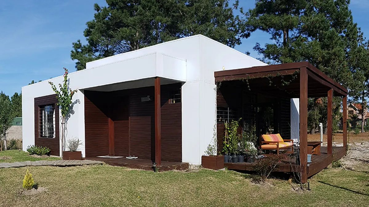 Vista exterior de la vivienda en El Pinar, con fachada clara y pérgola de madera junto al acceso.