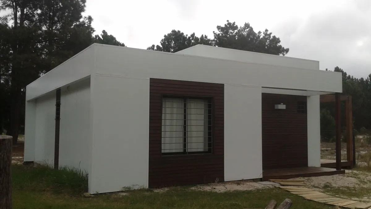 Vista oblicua de la vivienda en El Pinar, con fachada clara y revestimientos de madera junto a las aberturas.