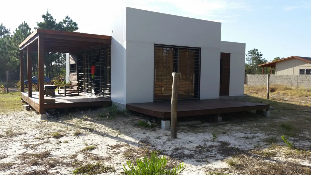 Vista general de la vivienda en El Pinar, con pérgola de madera, frente claro y recorrido exterior.
